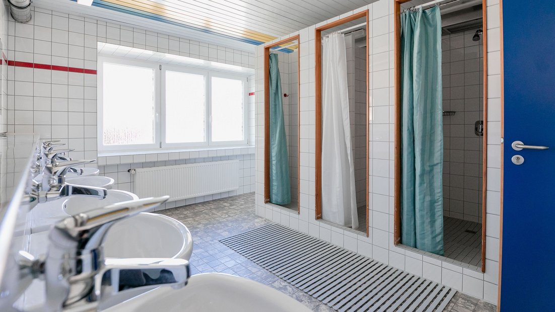 White tiled bathroom in the summerhouse with multiple sinks and showers