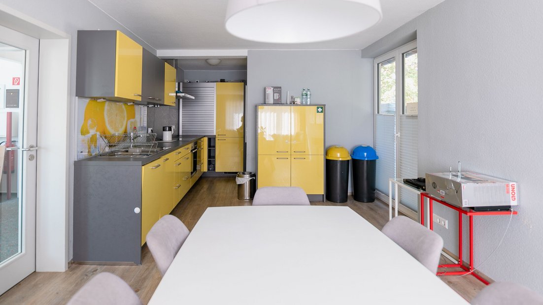 Modern kitchenette in grey-yellow with dining table group in the foreground