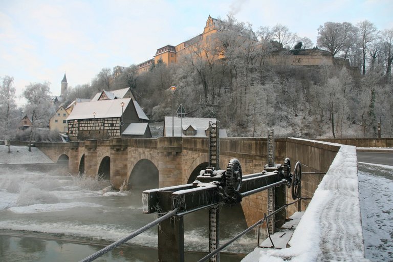 Winter view towards the stone bridge with round arches and weir on the Schloss-Berg Kirchberg