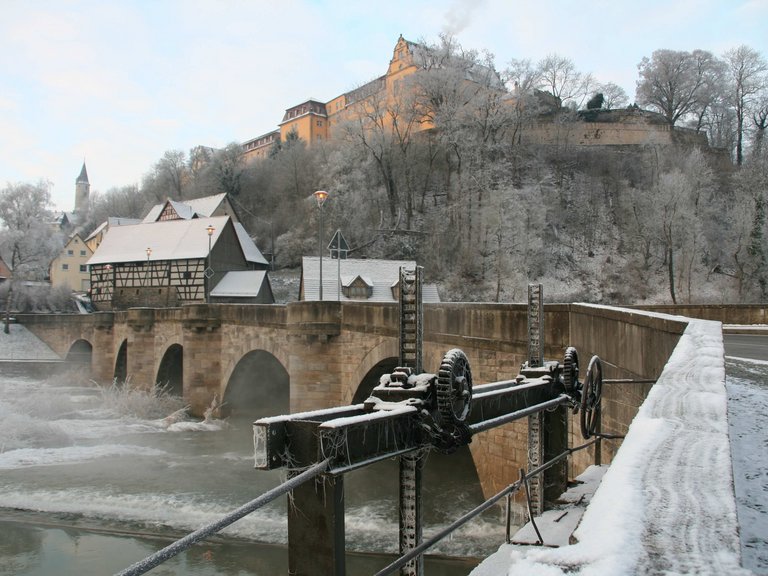 Winter view towards the stone bridge with round arches and weir on the Schloss-Berg Kirchberg