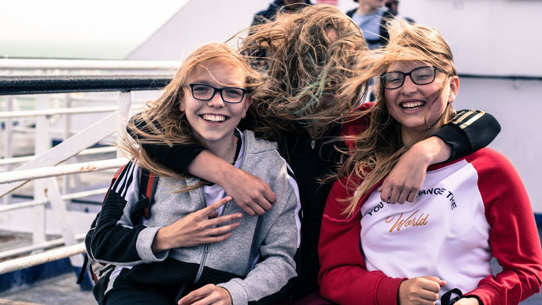 Three girls on the deck of a ship laugh into the camera.